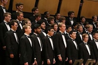 a group of men in tuxedos singing in a choir