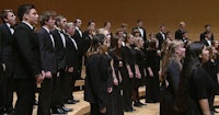 a group of people in tuxedos singing in a choir